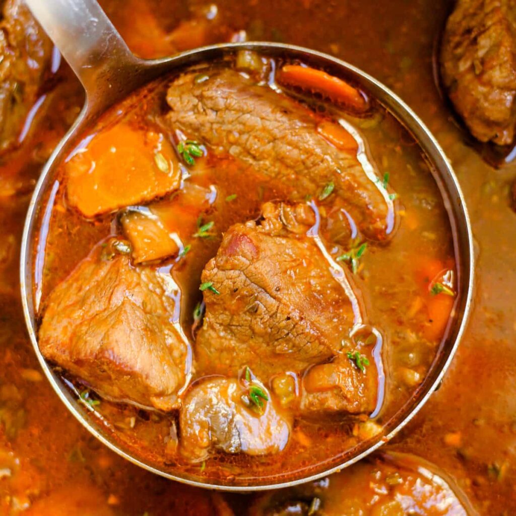 A ladle full of beef stew without potatoes.